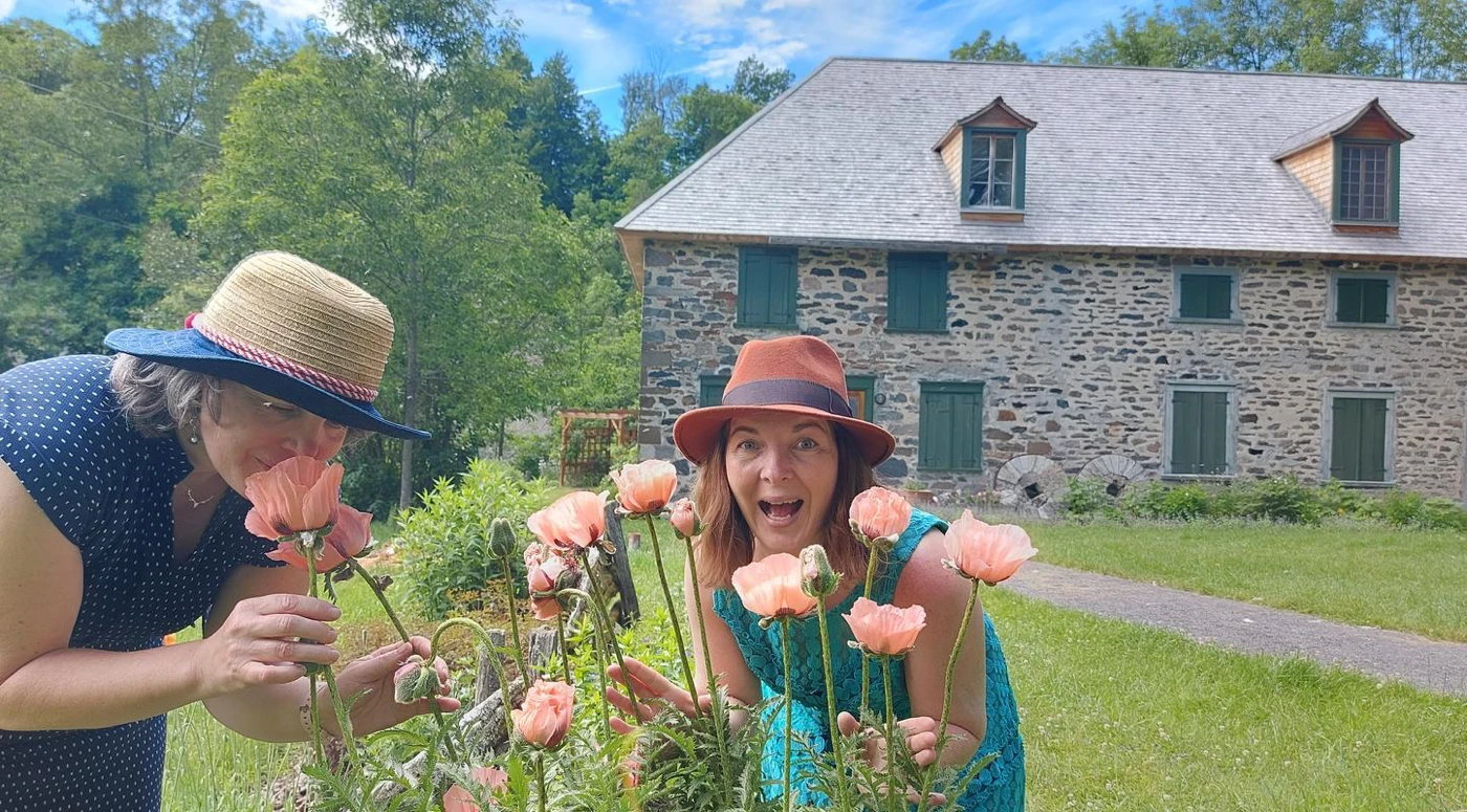 Deux femmes admirent des fleurs devant maison en pierre
