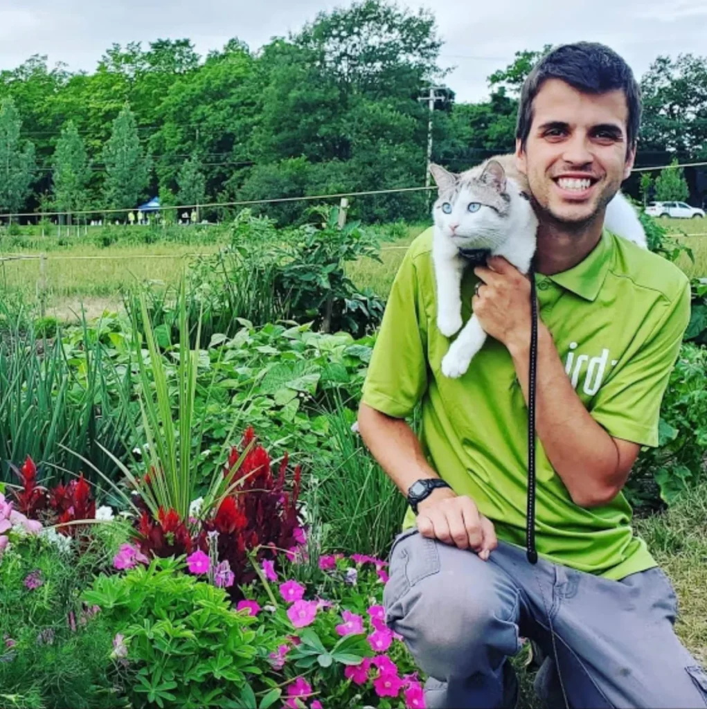 Homme souriant tenant un chat dans un jardin fleuri