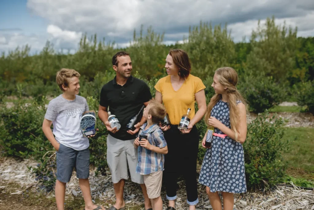 Famille dans un verger tenant bouteilles et myrtilles